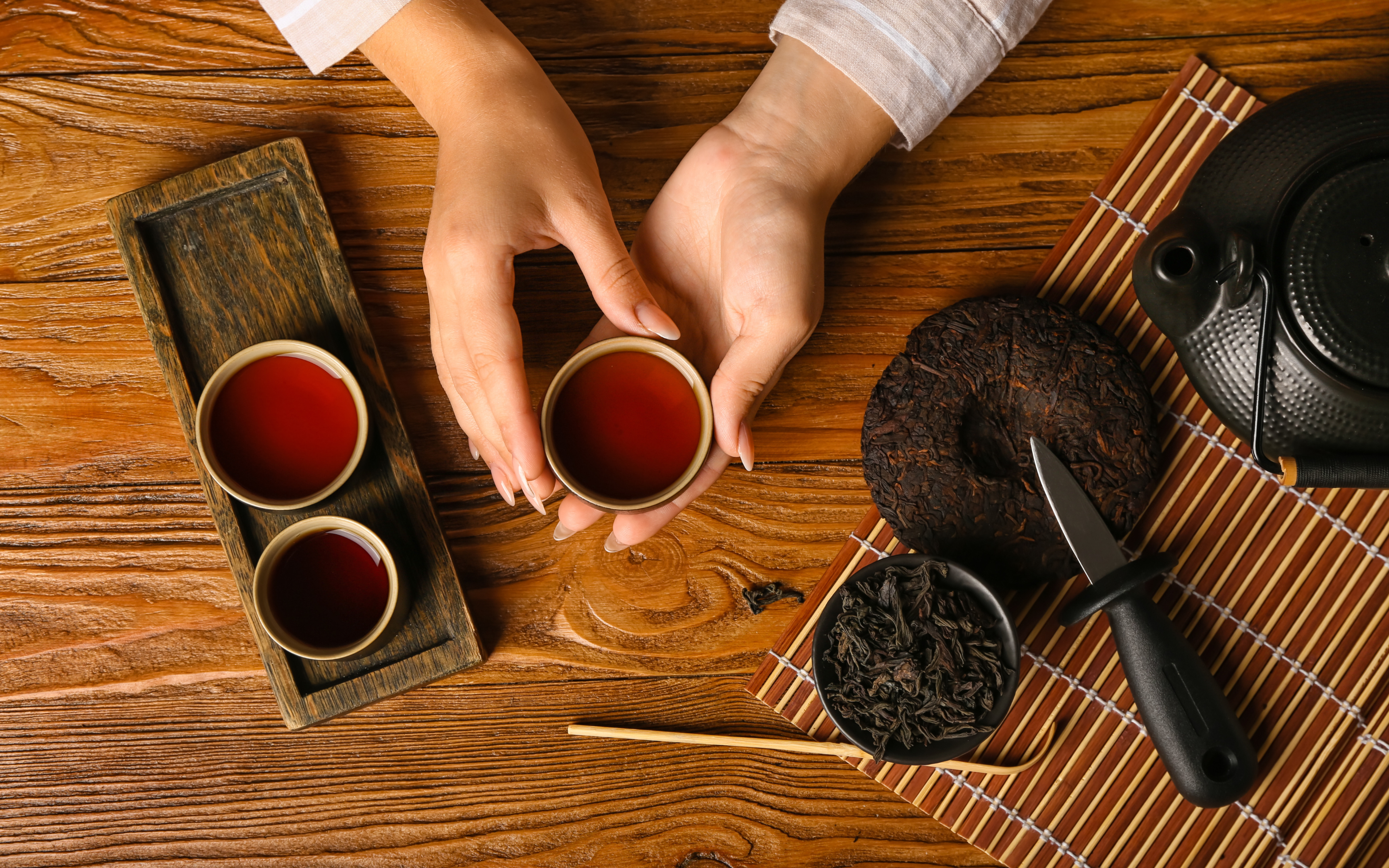 Female hands with cup of aromatic puerh tea on wooden background